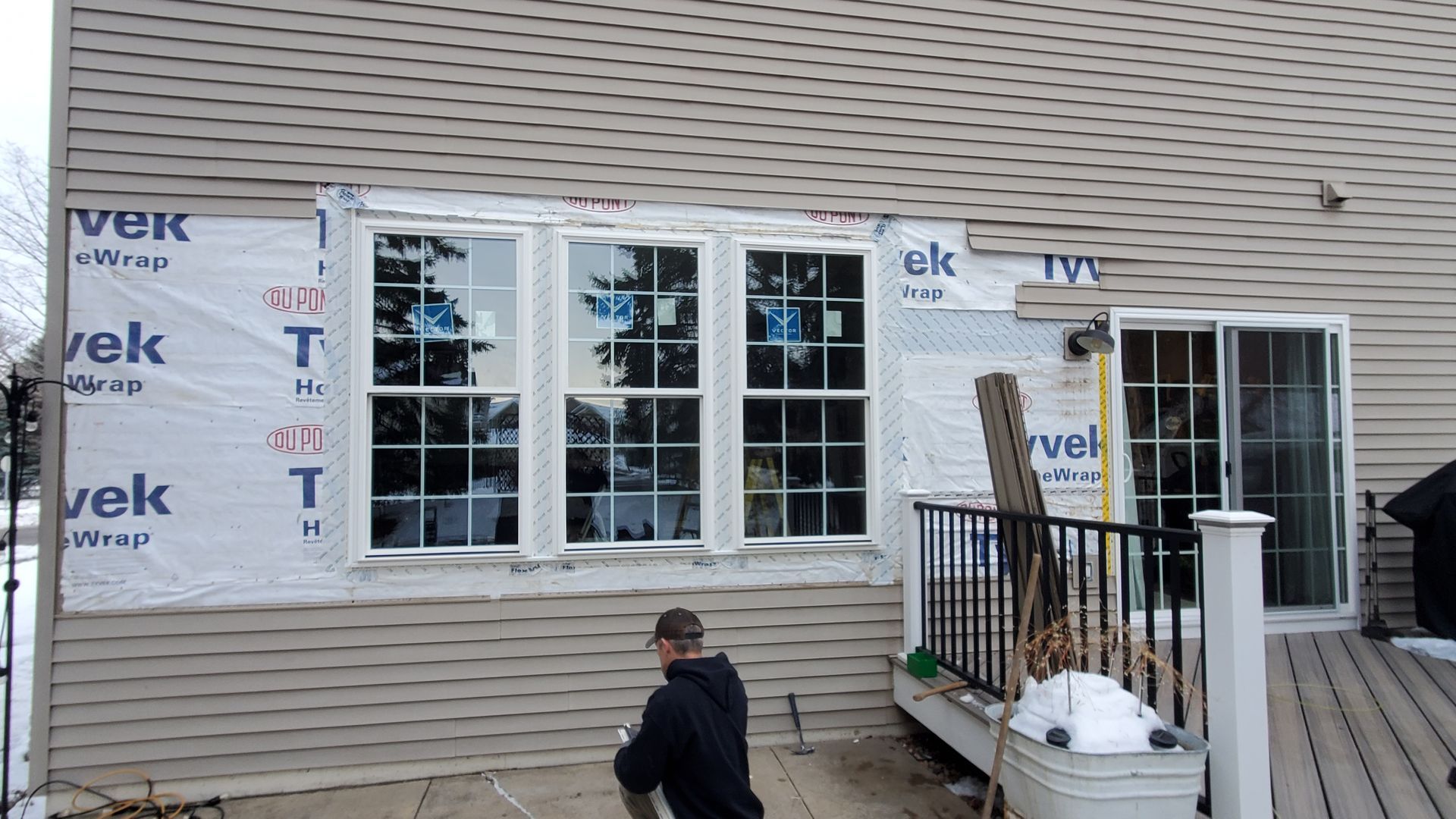 Exterior of a house under construction with new windows, siding wrap, and a person on the deck.