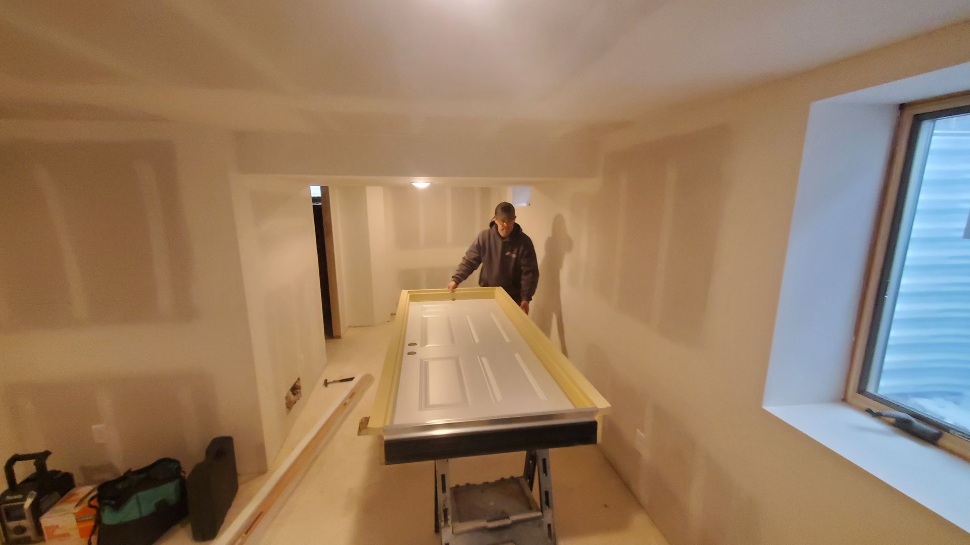 Worker in a narrow unfinished room moving a large white panel on a cart during renovation.