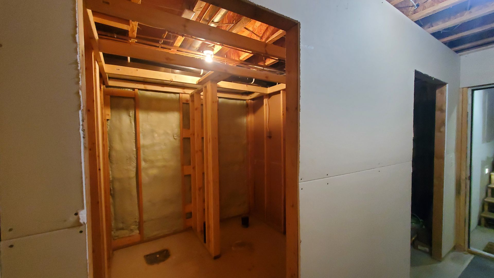 Unfinished home interior with exposed wooden framing and an open doorway to a hallway