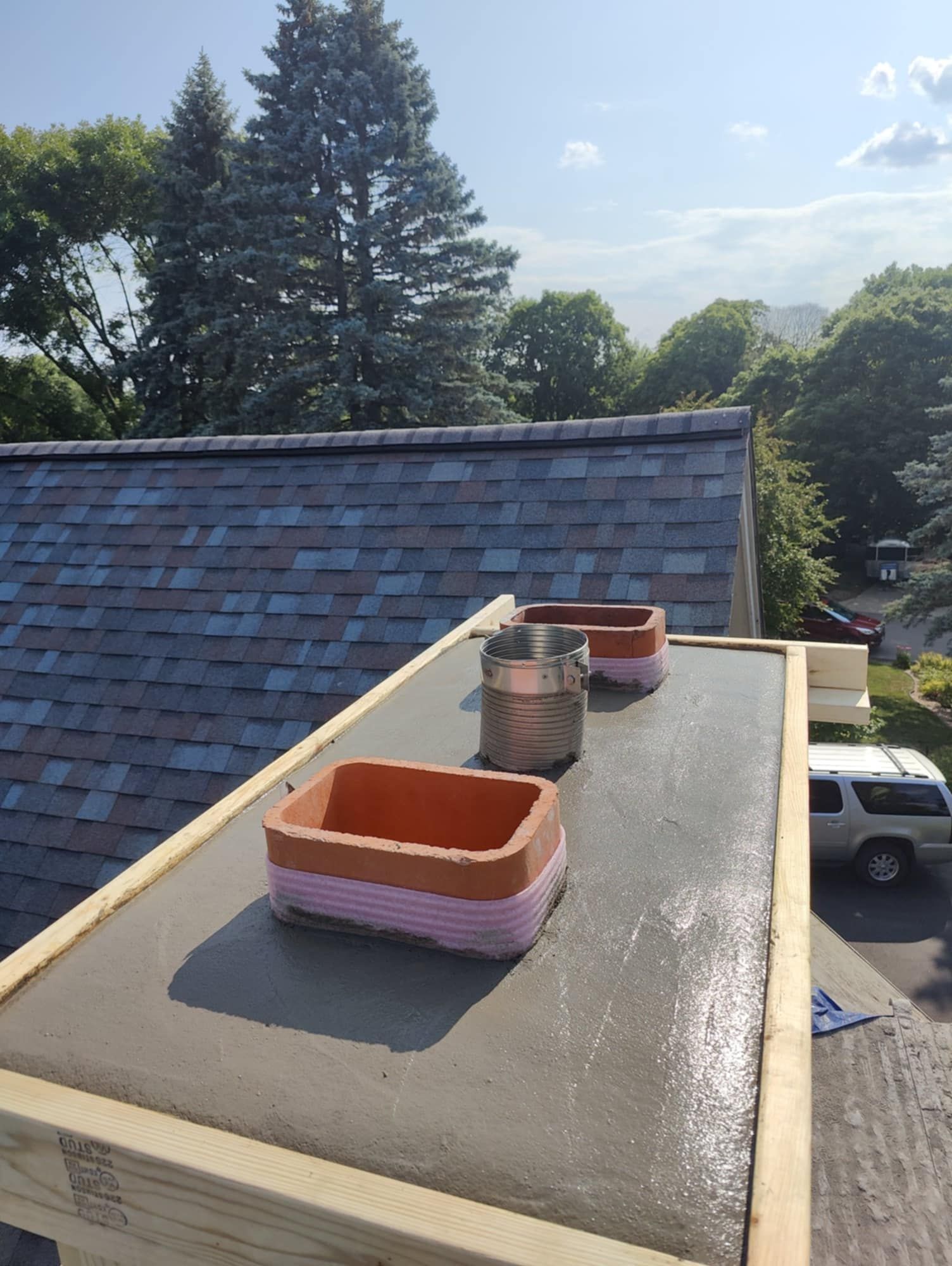 Rooftop with freshly coated black flat roof and two orange vent chimneys beside blue-shingled roof.