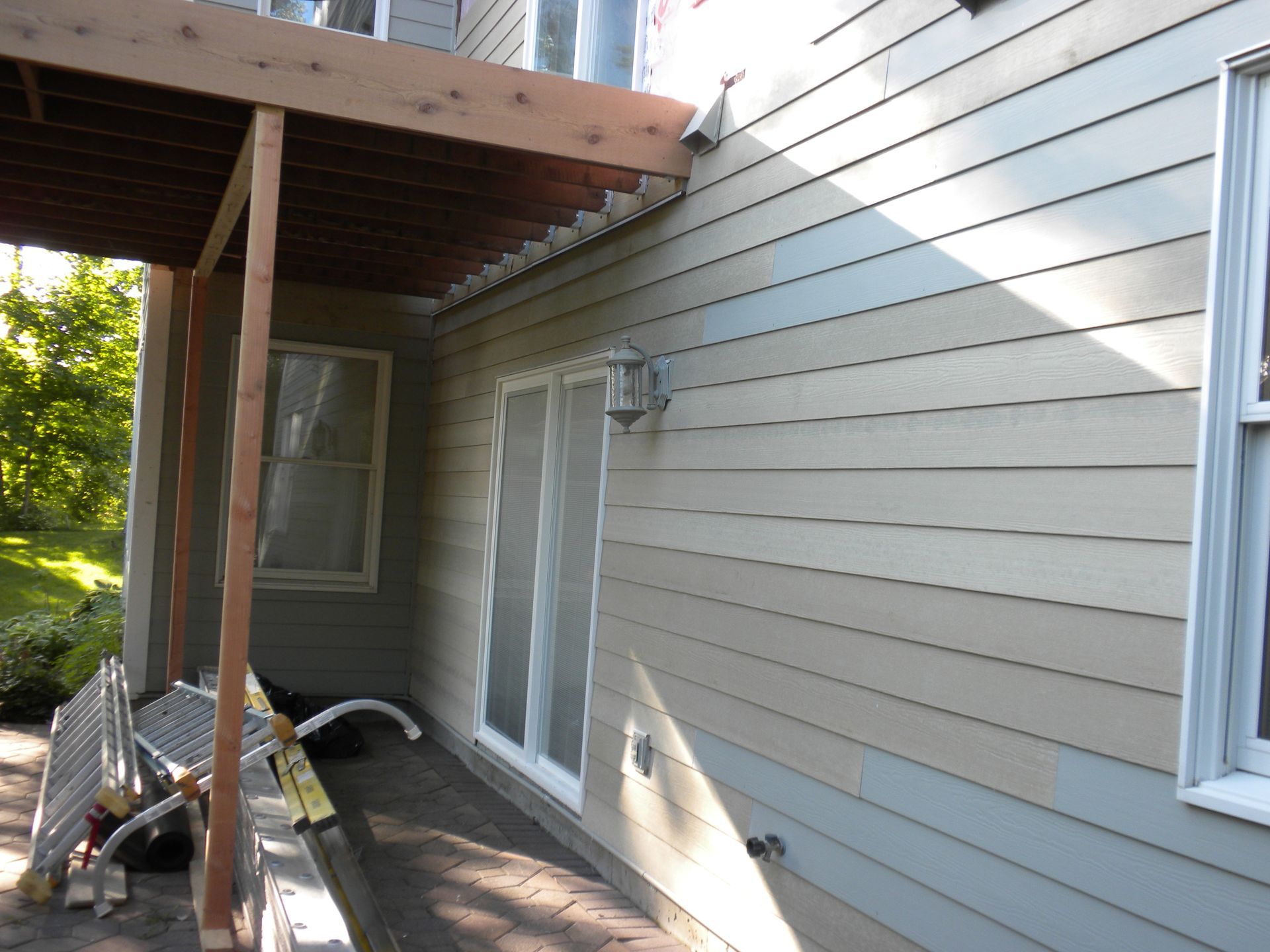Side of a gray house with a covered porch, windows, and construction materials along the wall.
