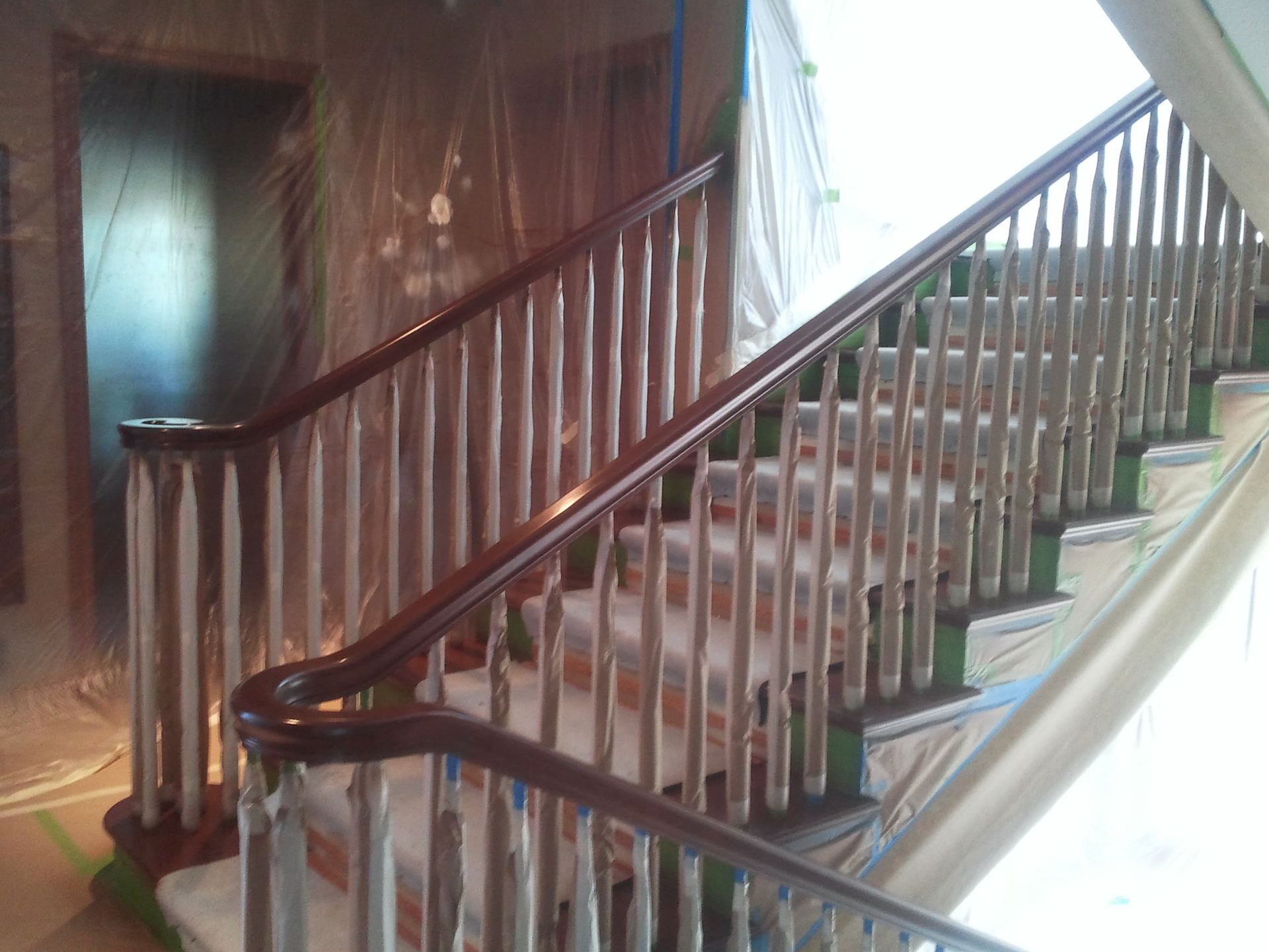 Wooden staircase with dark banister and white balusters in a sunlit interior.