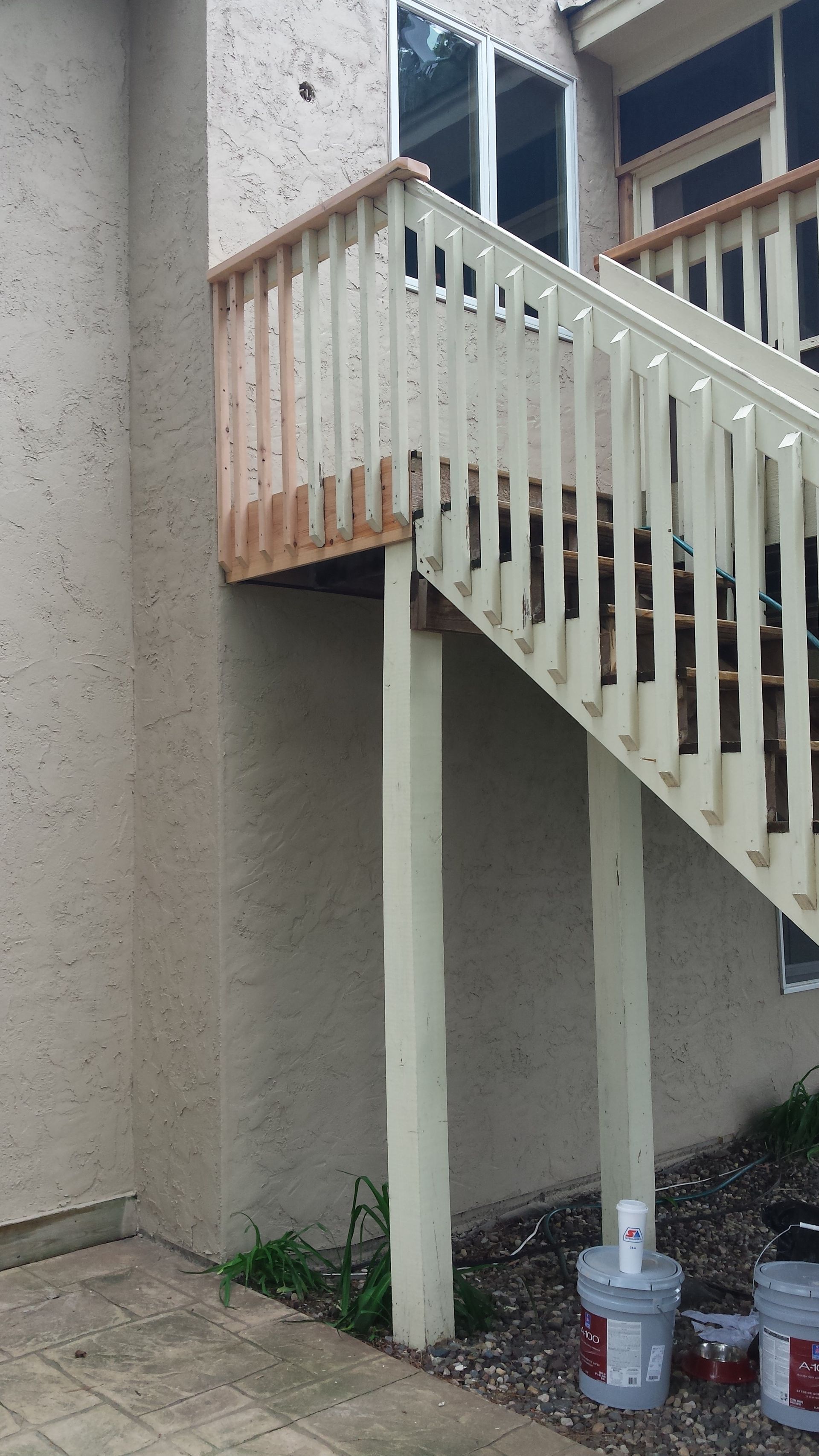 Exterior staircase with white railing beside a beige stucco building and paint cans on the ground.