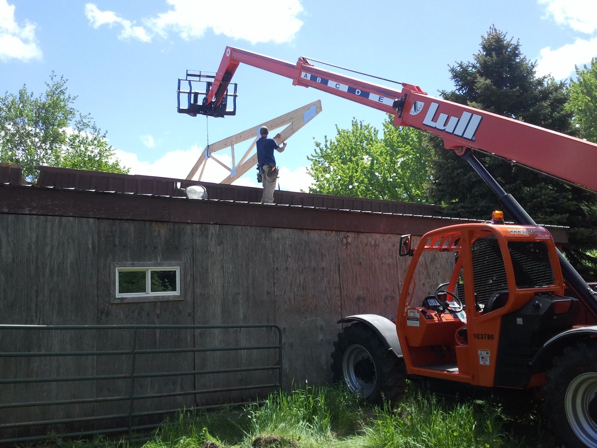 Worker on a red lift repairing a rooftop on a building beside a fenced yard.