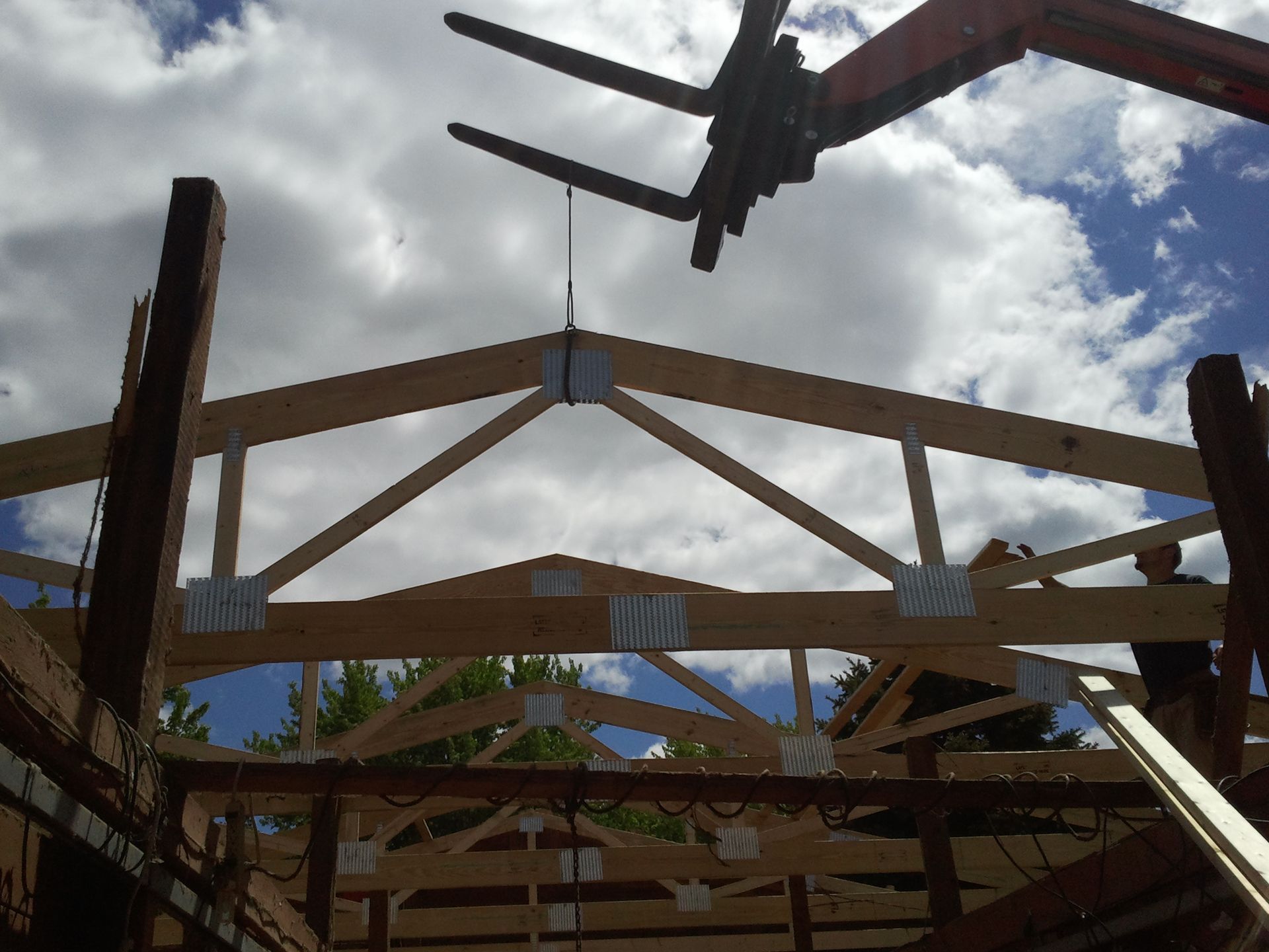 Wooden frame under construction against a cloudy sky, with a plane overhead.