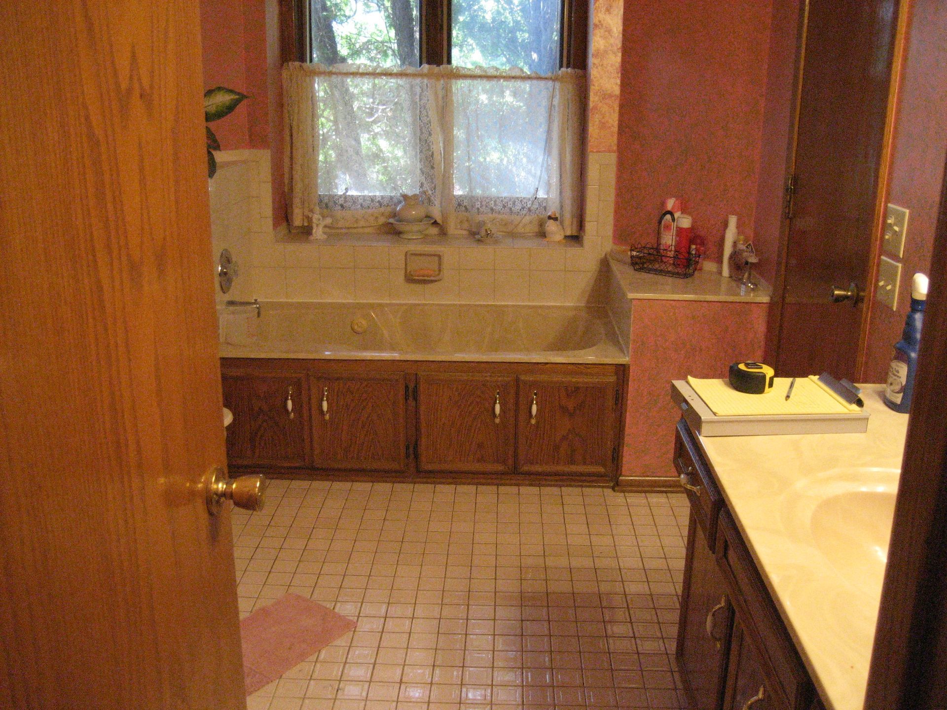 Empty kitchen with tan tile floor, wood cabinets, and a sink beneath a window.