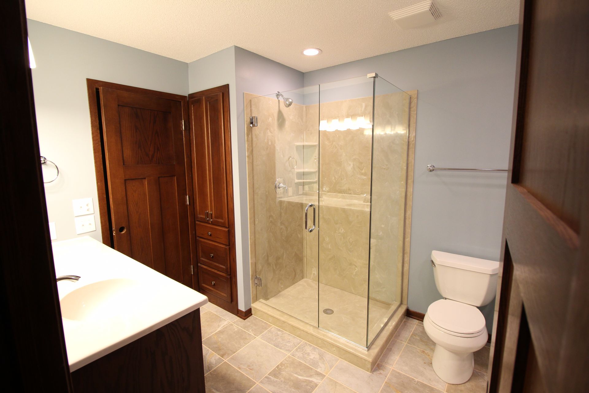 Modern bathroom with glass shower, toilet, double sink, and wood doors