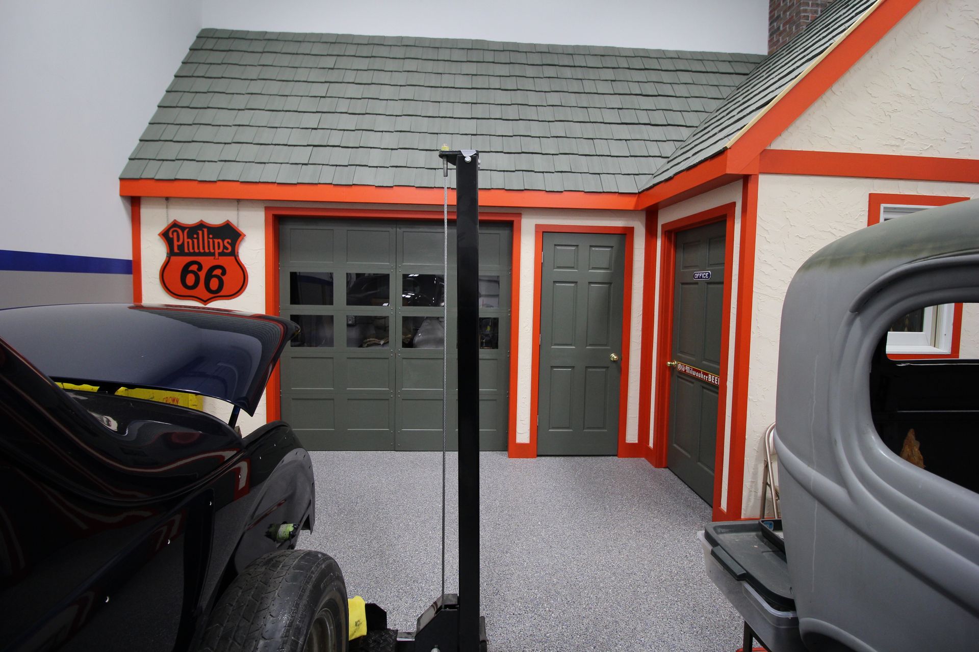 Custom Route 66 garage with gray door, orange trim, and vintage cars in the foreground