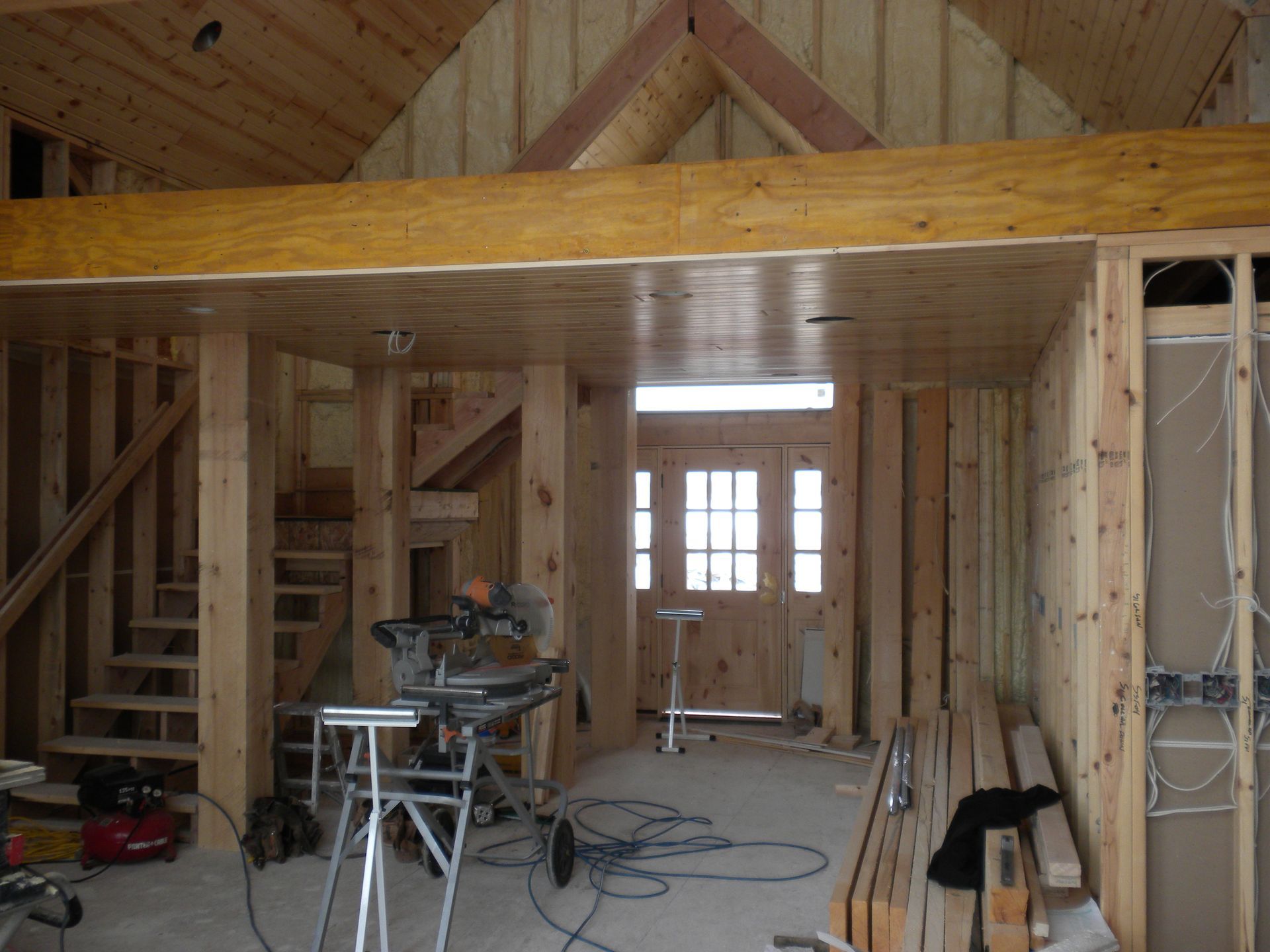 Wood-framed interior under construction with stairs, tools, and exposed beams