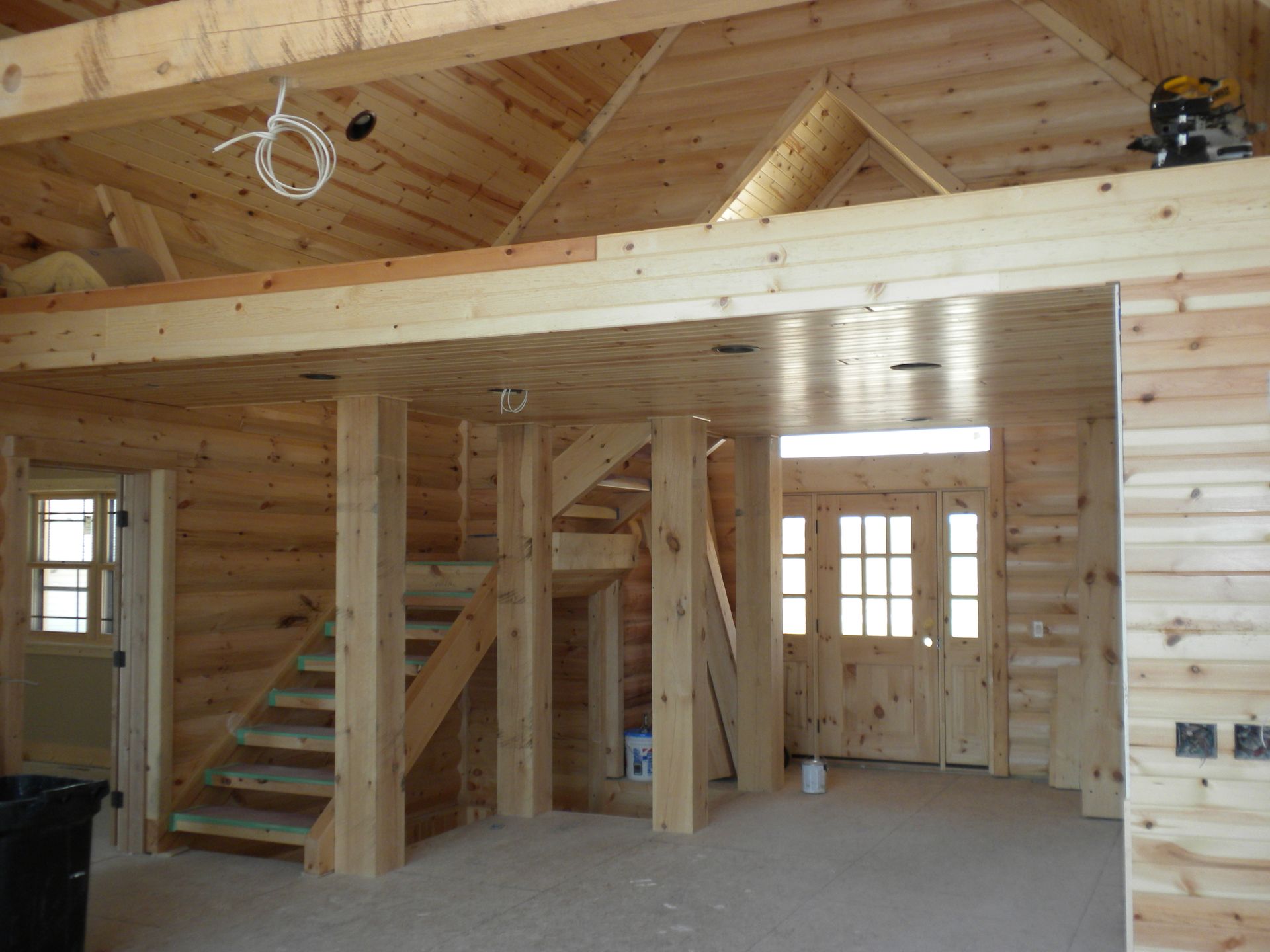 Interior of a unfinished wooden house with exposed beams, staircase, and loft area