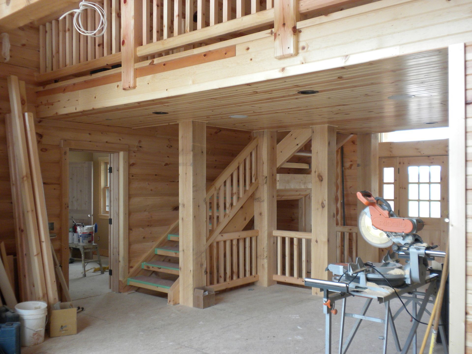 Wooden home interior under construction with stairs, loft, and a miter saw in the foreground