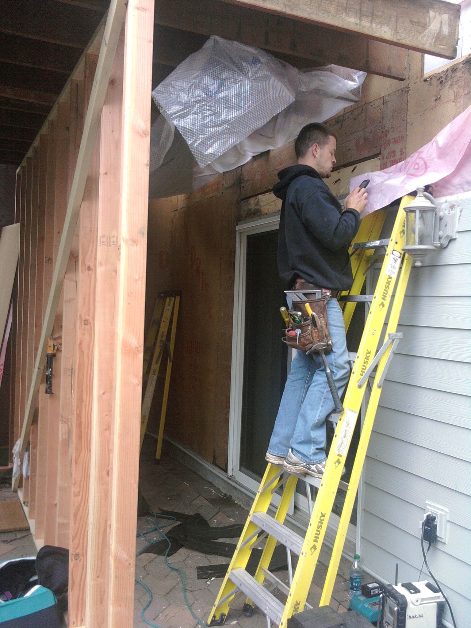 Worker on yellow ladder repairing exterior wall and soffit under a porch overhang.