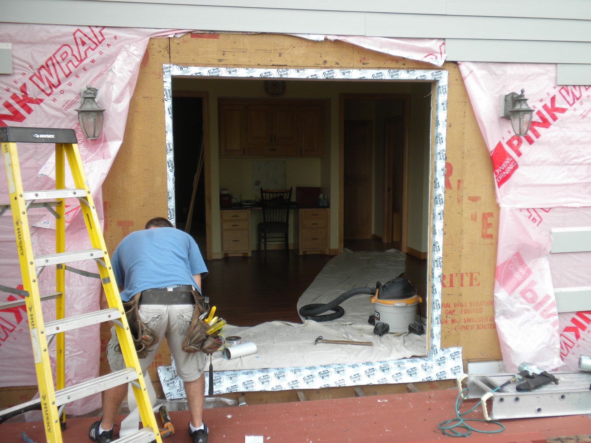 Worker installing trim around a large doorway opening in a partially renovated building