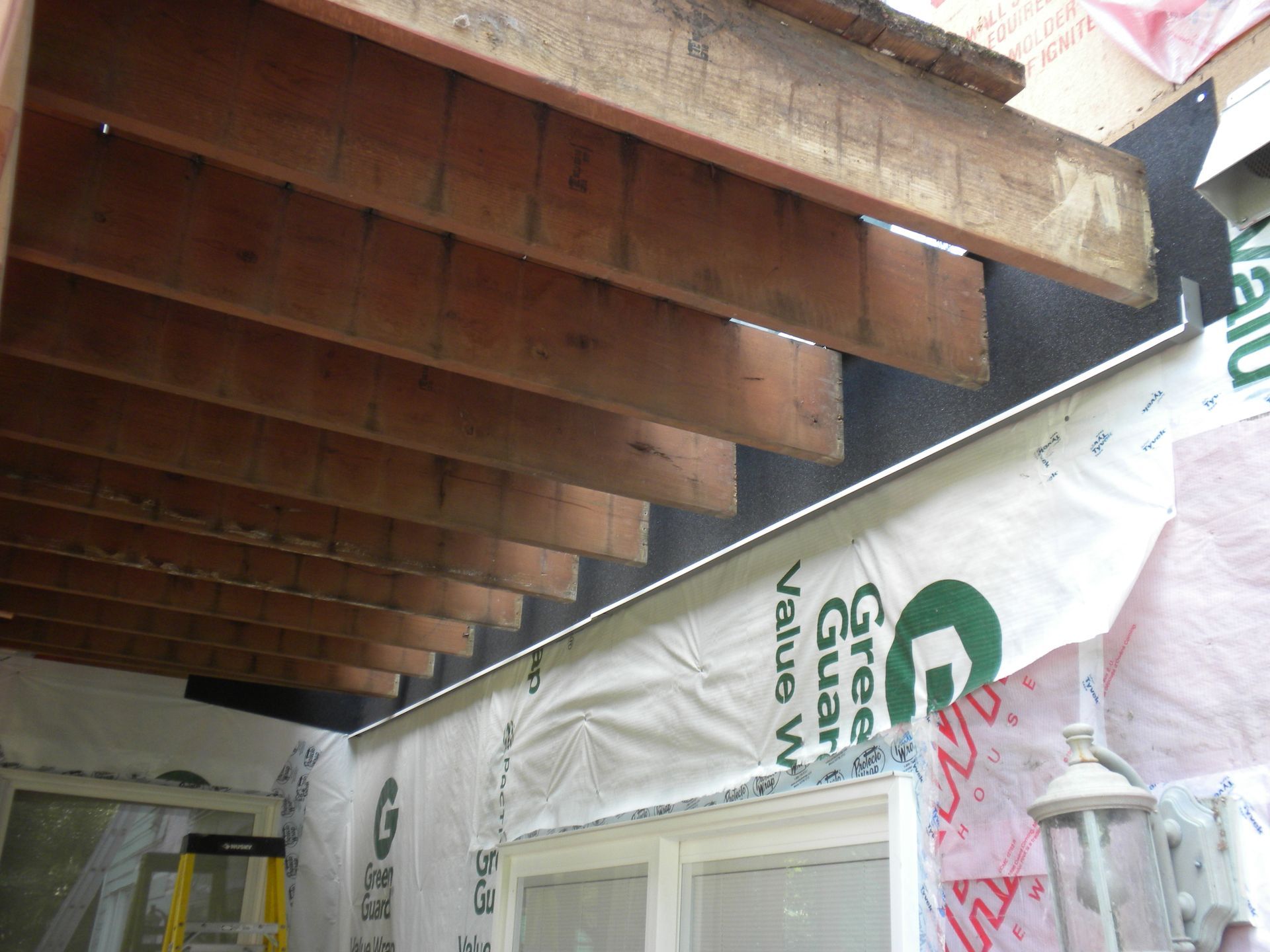 Exposed wooden ceiling joists above wrapped wall sheathing and a window opening in a construction area