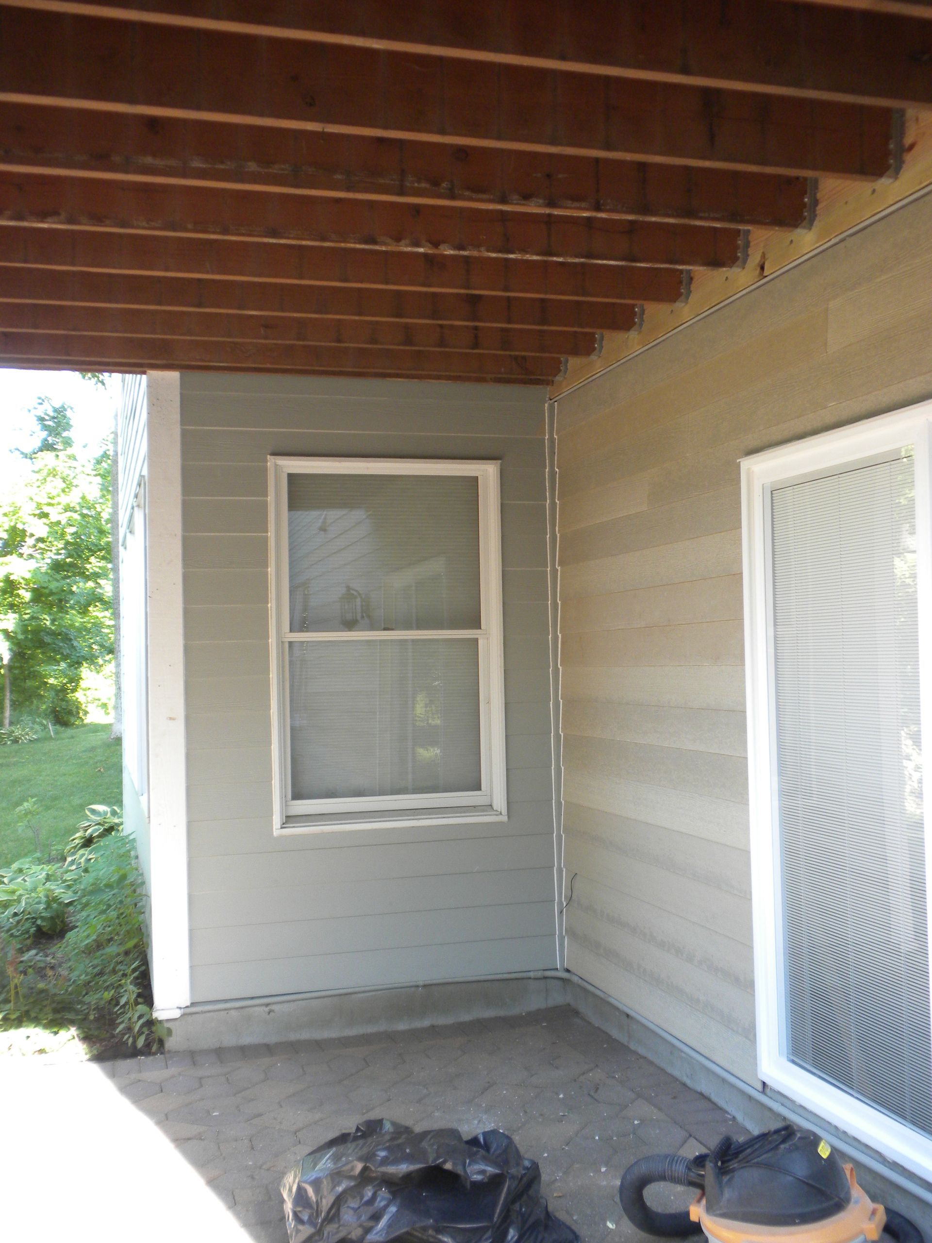 Covered porch with wood ceiling, gray siding, a window, and a white screen door.