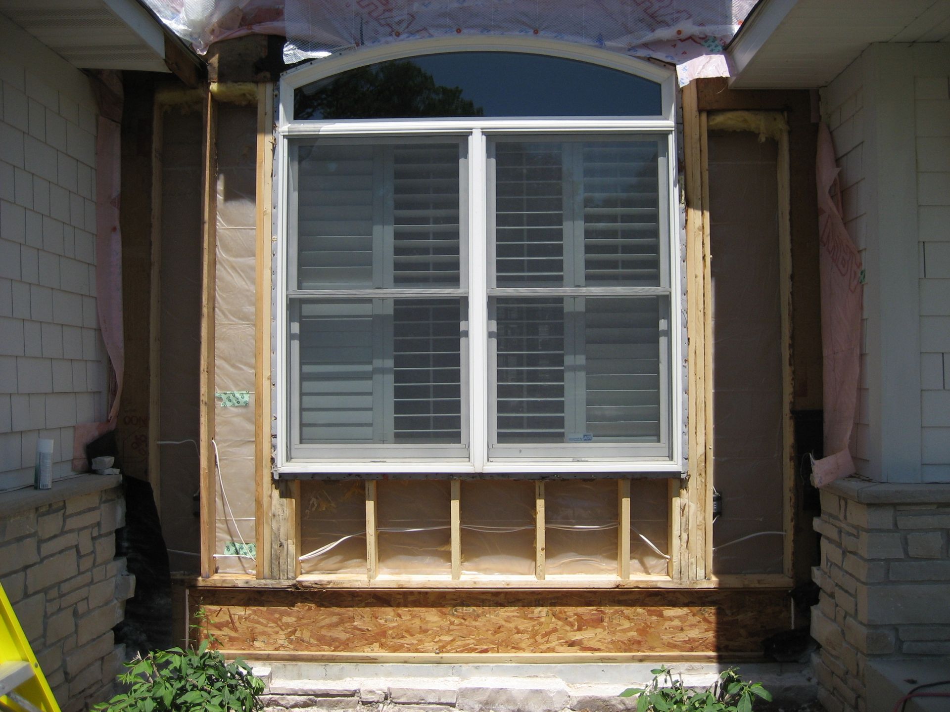 Window framed by unfinished wooden siding under a stone archway on a house exterior