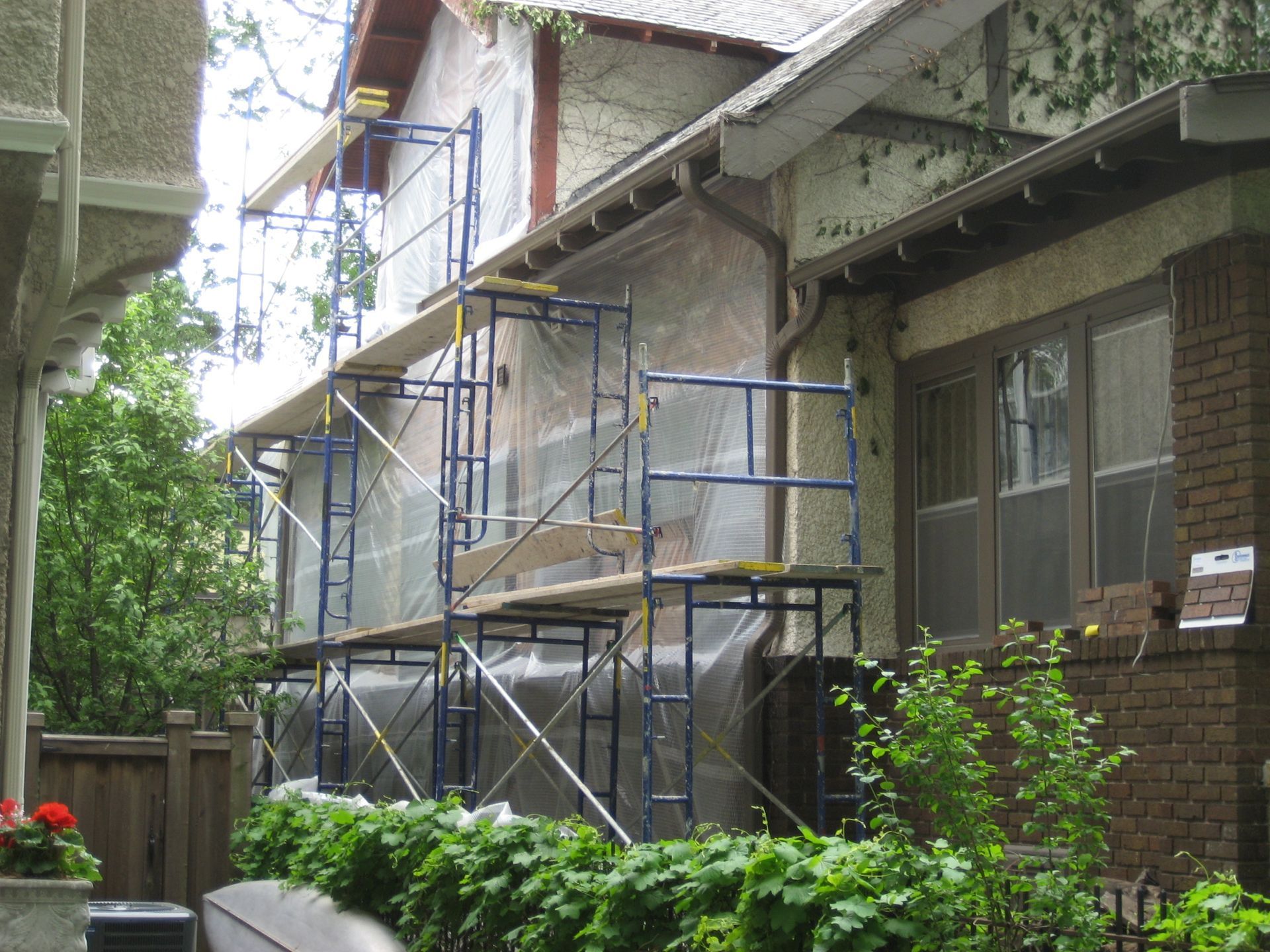 Scaffolding around a brick townhouse exterior with covered walkways and shrubs in front