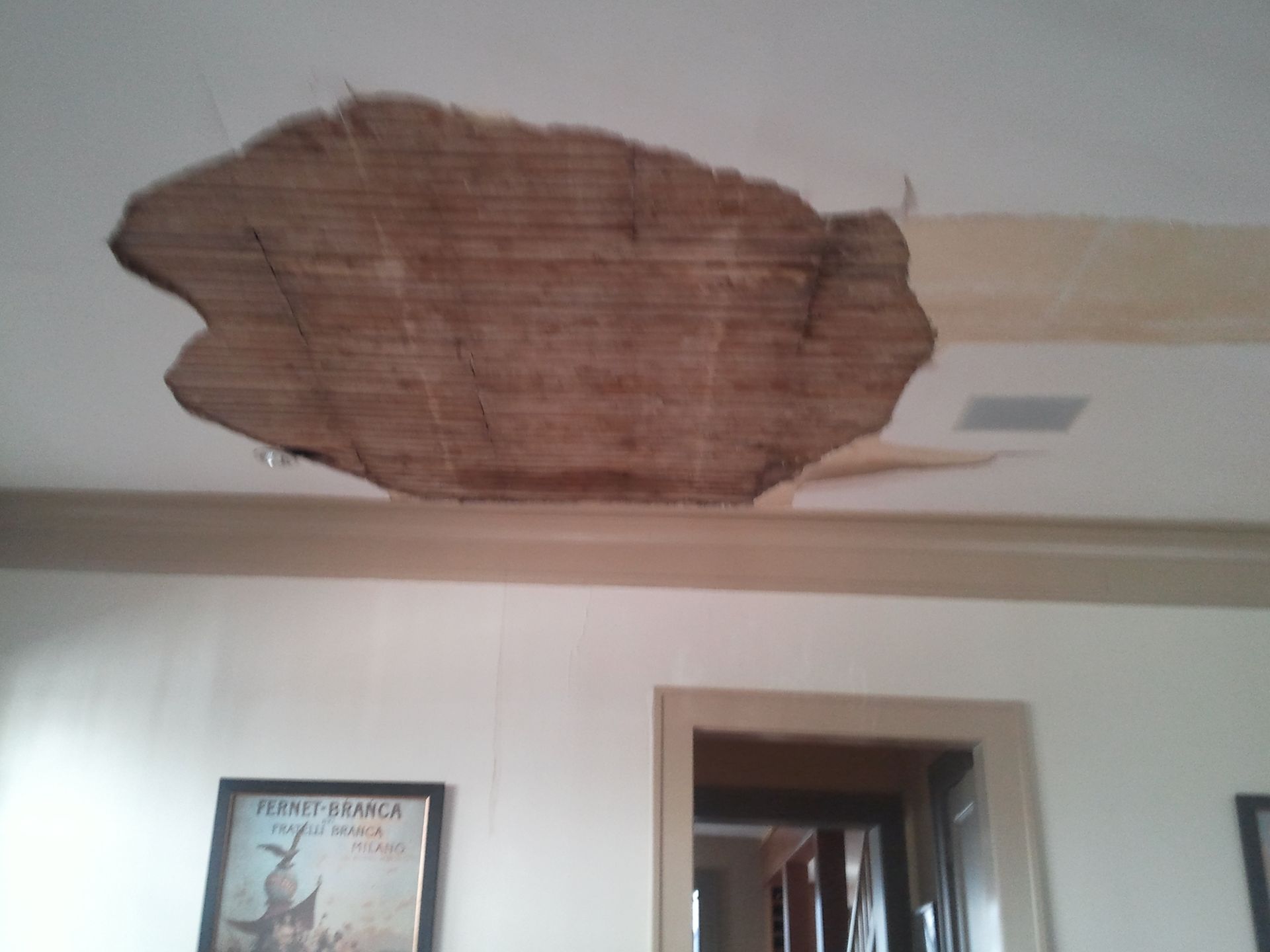 Damaged ceiling with exposed brown insulation above a doorway in a white room