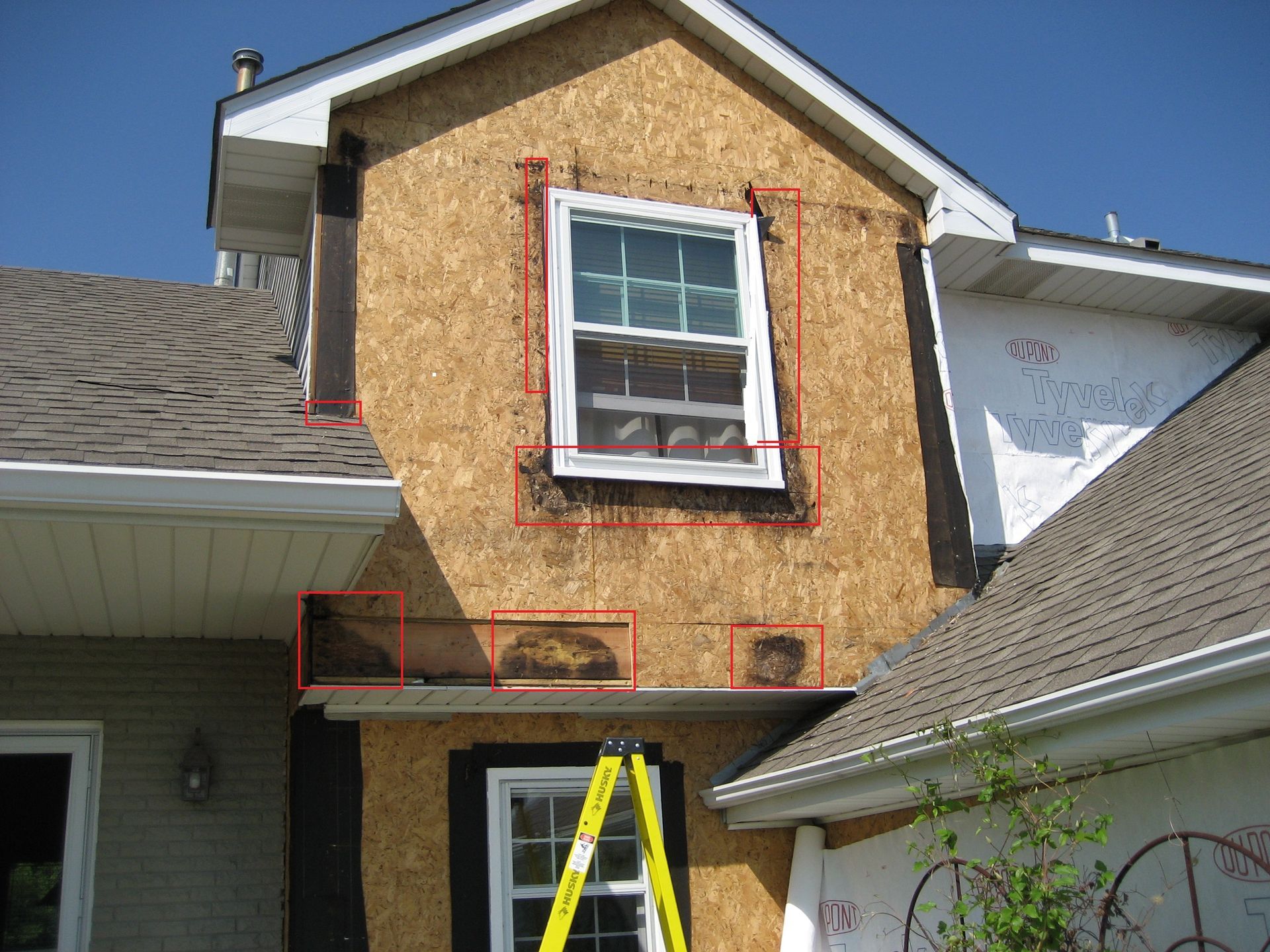 House exterior with a ladder leaning against a small upper window and red trim markings around the facade