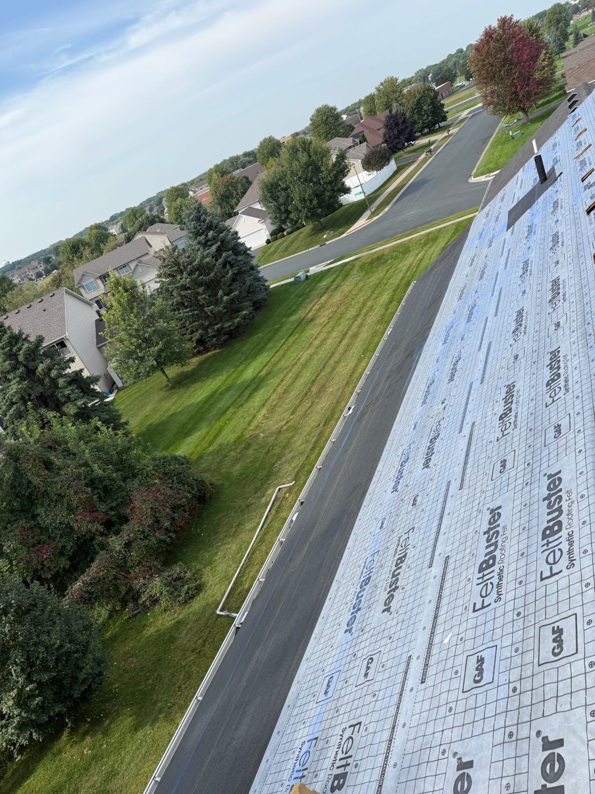Roof with underlayment beside a suburban street and grassy yard on a clear day