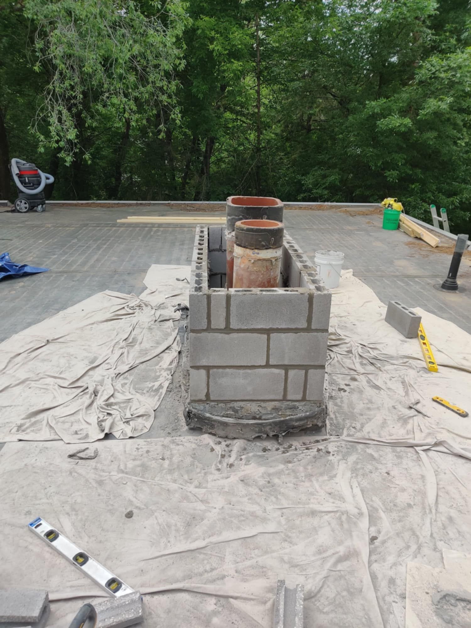 Brick chimney under construction on a tarp-covered rooftop with tools nearby.