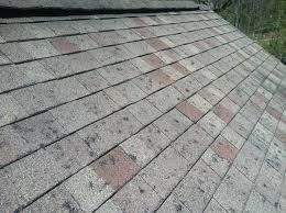 Close-up of weathered gray shingle roof with scattered reddish stains and moss at the edge