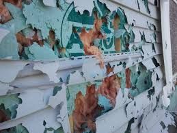 Peeling white exterior paint with exposed teal and rust-colored layers on a weathered wall