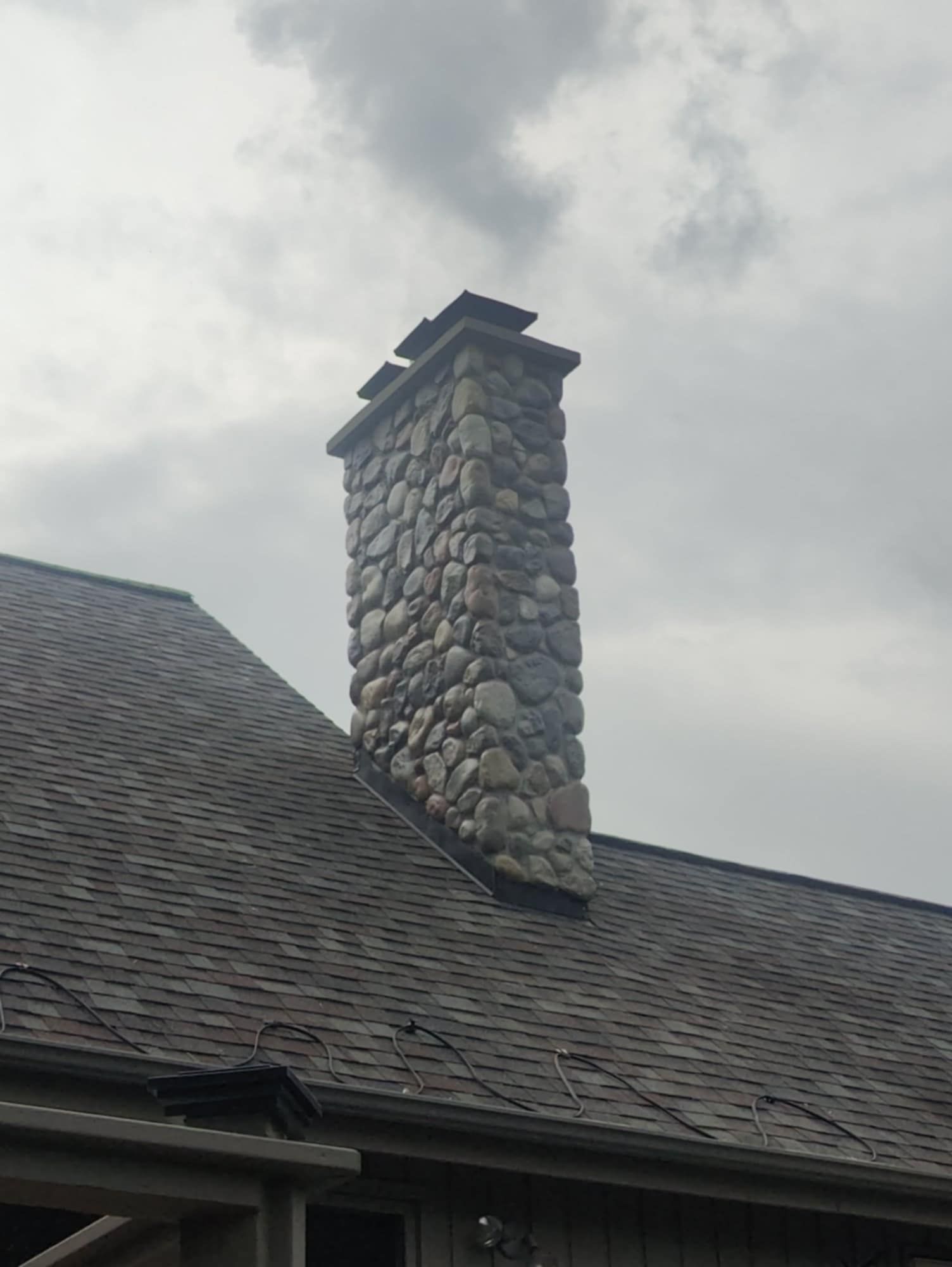 Stone chimney on a shingled roof against a cloudy sky.