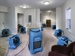 Room with several blue portable fans on the floor and a table turned upside down in the center.
