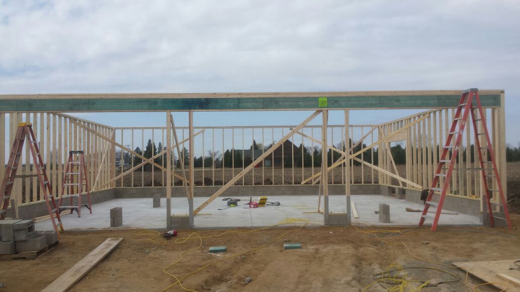 Construction site with concrete foundation, steel framing, and red scaffold supports under a partly built roof