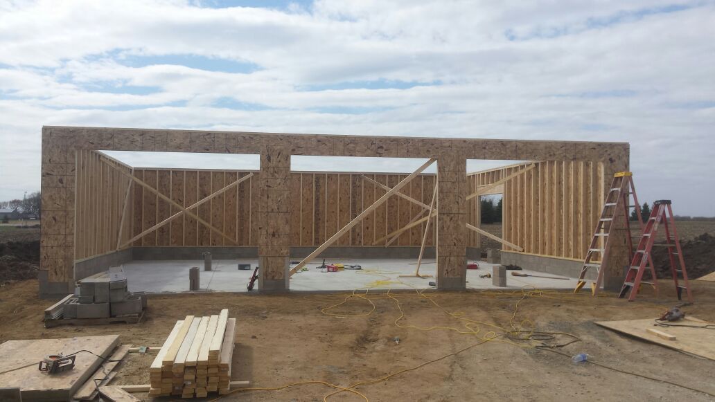 Partially built wooden house framing at a construction site with ladders and lumber on the ground