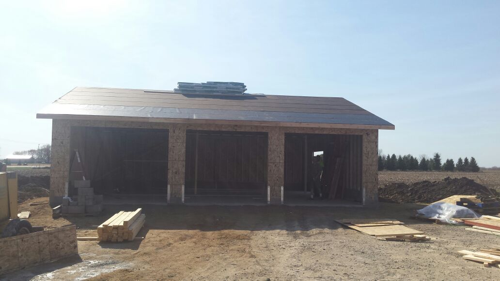 Small unfinished brick house with open window and door frames on a dirt lot under a bright sky.