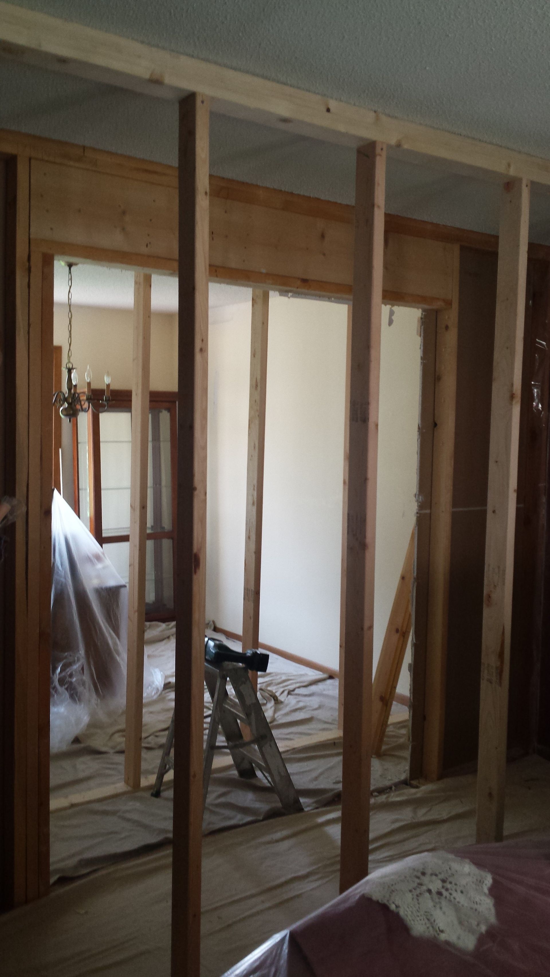 Exposed wooden studs in an unfinished room with construction tools and a ladder near a window.