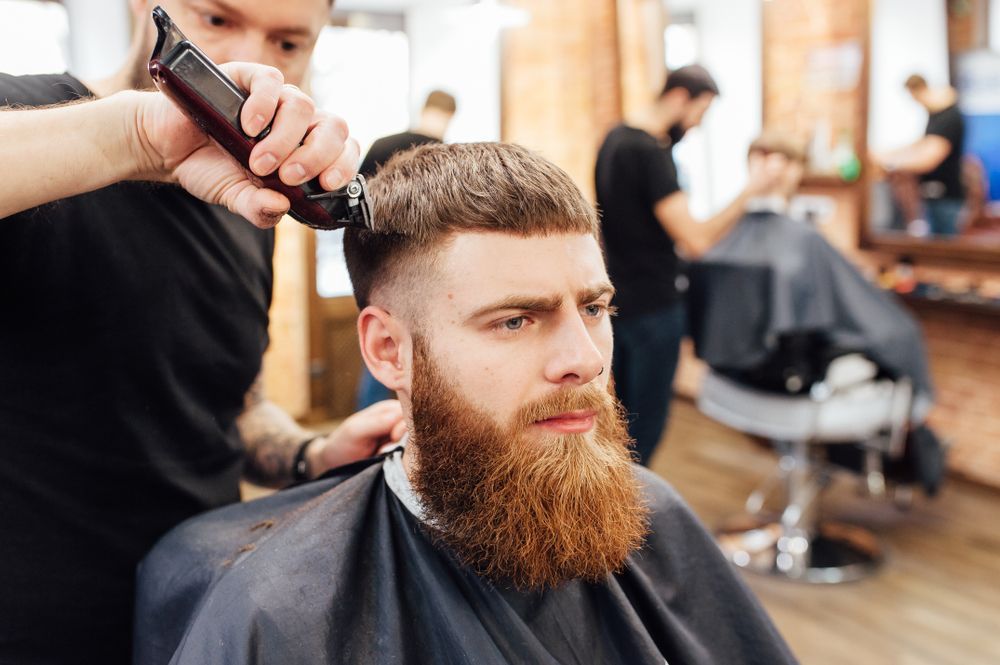 A Man With a Beard is Getting His Hair Cut by a Barber in a Barber Shop — Barbarella Hair in Maryborough, QLD