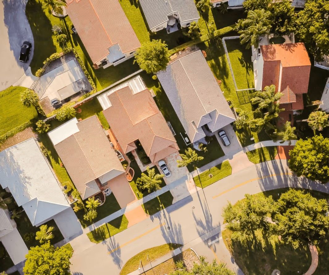 An aerial view of a suburban neighborhood showing several residential homes with tiled roofs and surrounding trees.