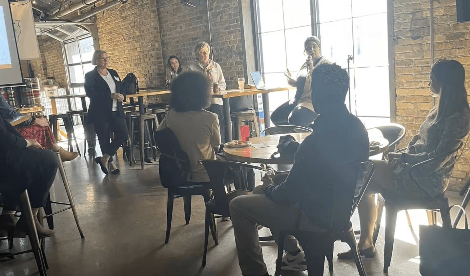 A panel of speakers sitting at a table in a rustic, brick-walled venue, facing an audience in an informal setting.