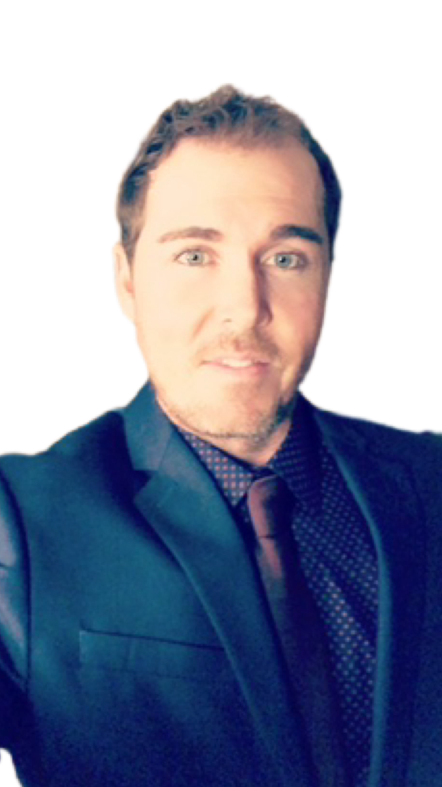 A smiling person with short, light brown hair wears a white button-down shirt and a blue plaid blazer against a white backdrop.