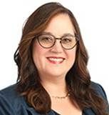 A professional headshot of a person with shoulder-length brown hair, wearing glasses and a dark blazer, smiling.