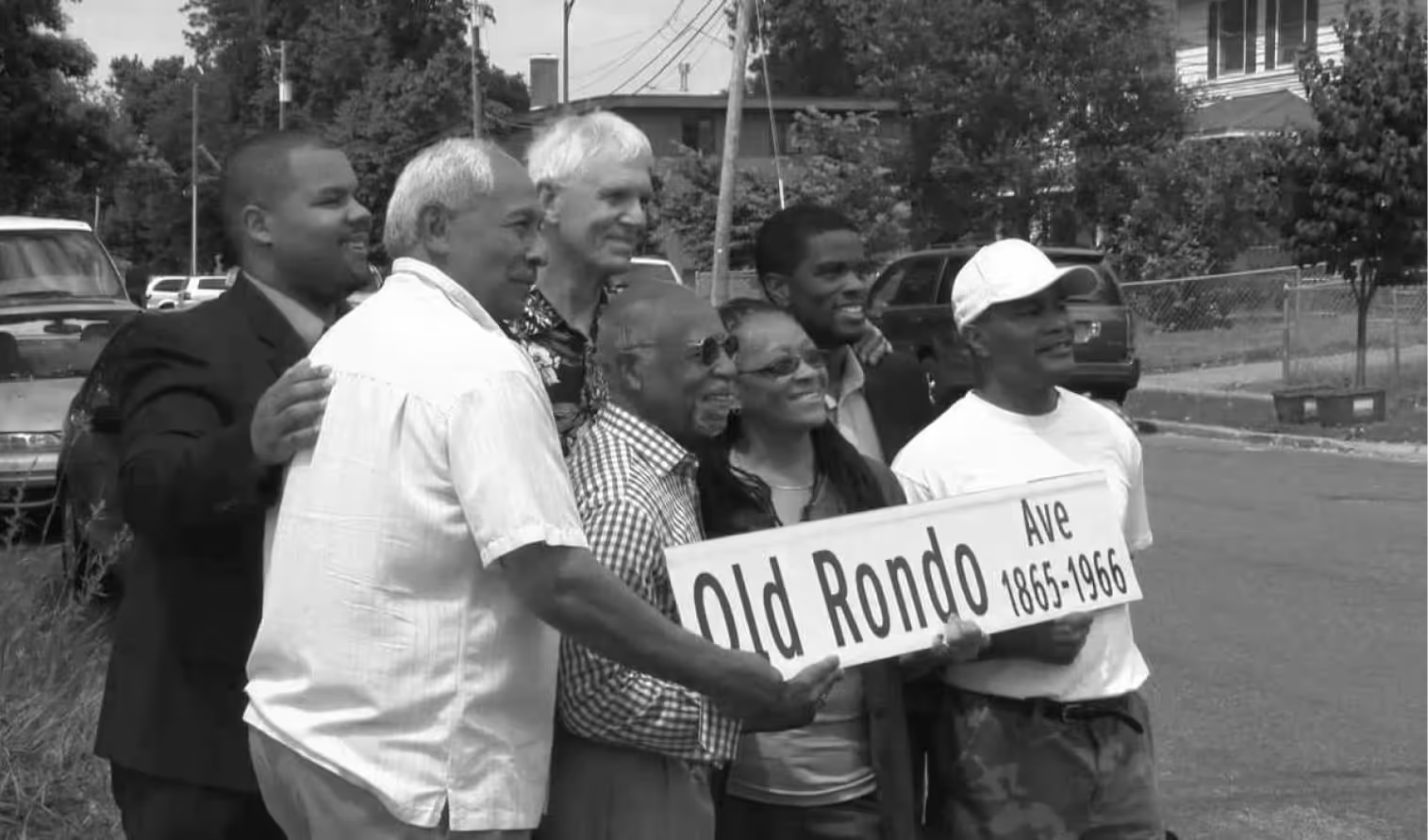 A group of people standing outdoors holding a street sign that reads