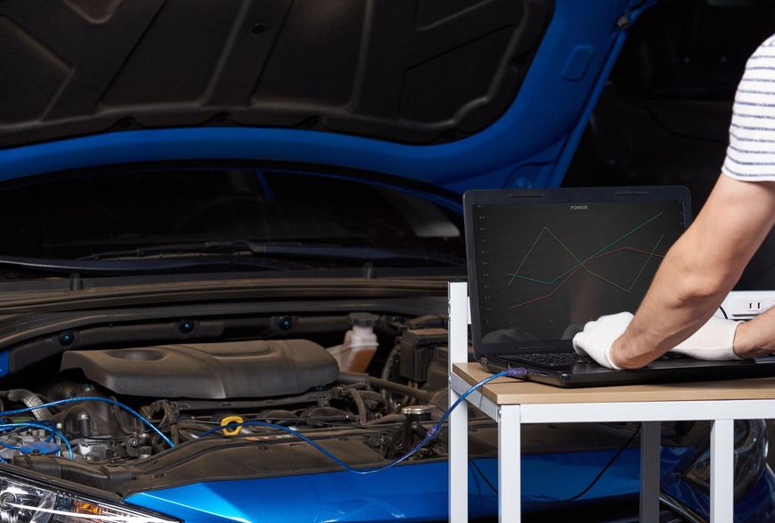 Vano motore dell'auto aperto con un computer portatile su un tavolo mentre un meccanico lavora nelle vicinanze