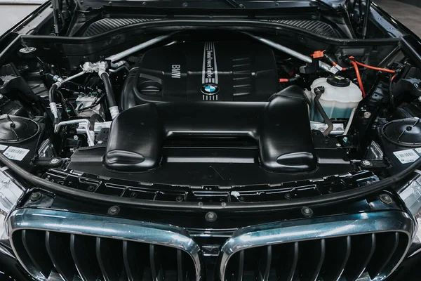 Vano motore dell'auto con copertura nera, bordo della griglia cromato e serbatoio del fluido visibile sotto il cofano