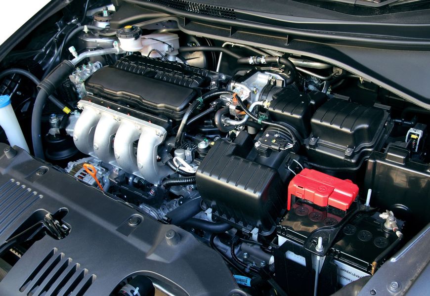 Vano motore dell'auto con componenti neri e collettore di aspirazione argentato, coperchio della batteria rosso visibile