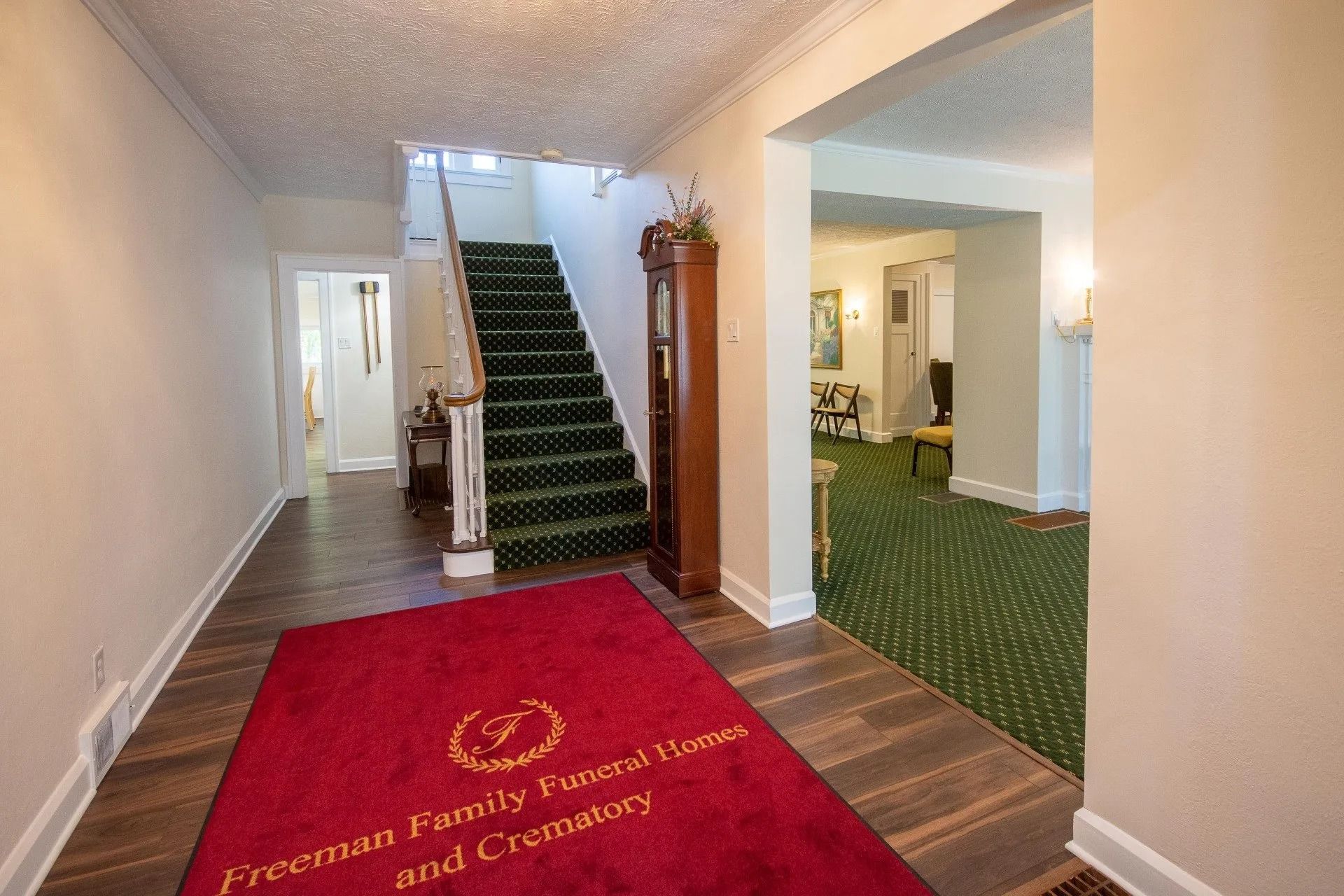 Red carpet with logo leads into funeral home hallway with stairs and clock.