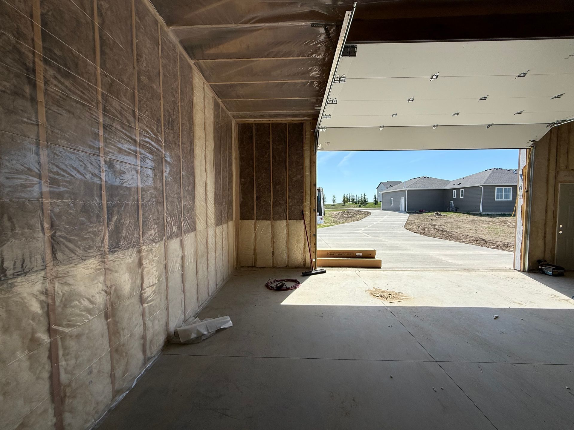 Interior of a garage under construction with insulation and a view of houses and road outside.