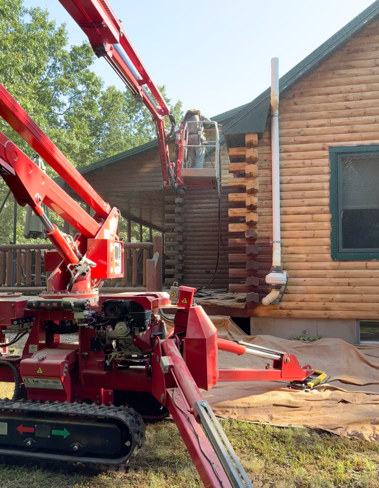 A red crane is sitting in front of a log cabin.