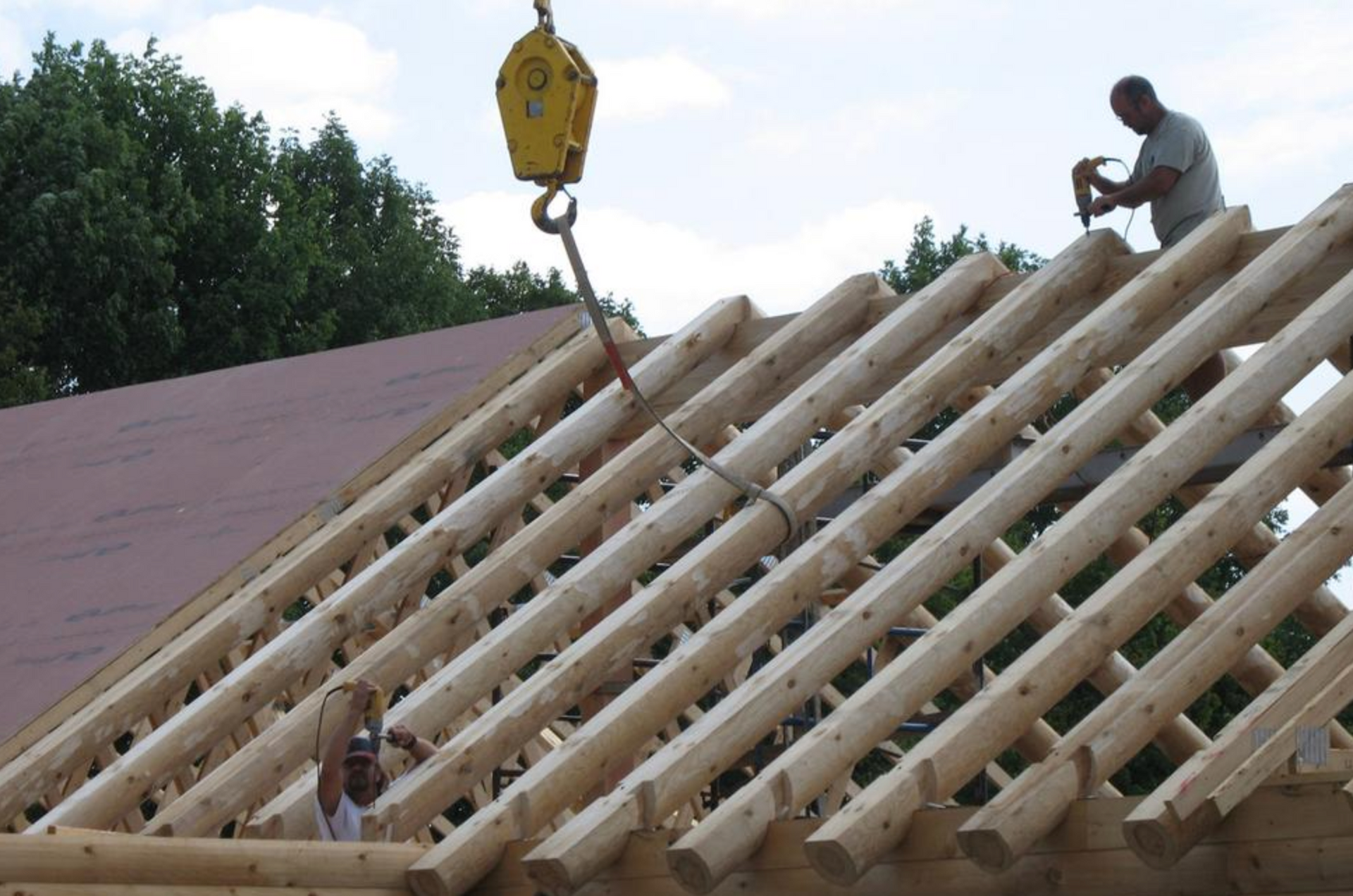 Two men are working on a wooden roof with a yellow crane