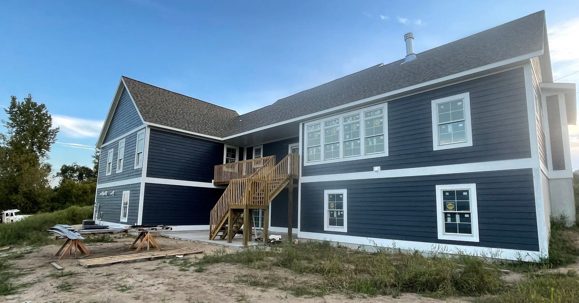 Blue-gray house with white trim and unfinished front porch under construction on a sandy lot