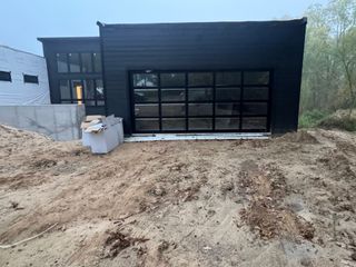 Black garage or workshop with glass door beside a dirt lot and construction materials.