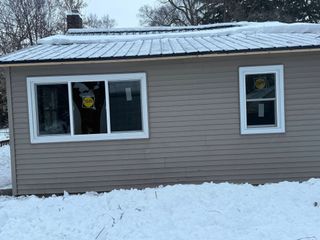 Snow-covered beige house with white-trim windows and a metal roof, seen in winter.