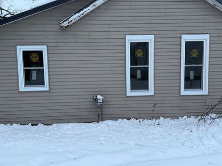 Snow-covered house exterior with three white-trimmed windows and beige siding